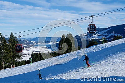 OBERSTAUFEN, GERMANY - 31 DEC, 2017: Ski lift with gondola and ski slope and skiers in the foreground Editorial Stock Photo