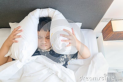 Obese boy lying in bed covering head with pillow because too loud annoying noise. I Stock Photo