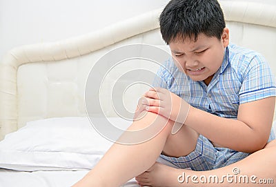 Obese boy suffering from knee pain and sit on bed, Stock Photo