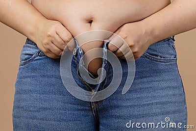 Obese lady with big abdomen trying to zip up jeans of blue colour. Visceral fat. Body positive. Sudden weight gain Stock Photo