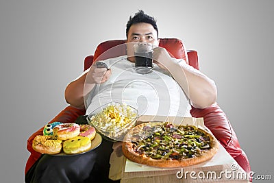 Obese man drinking and overeating on the sofa Stock Photo