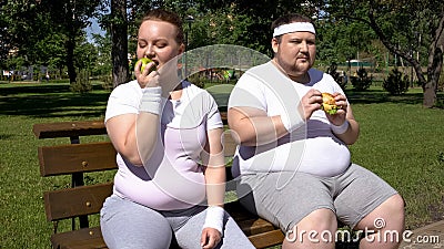 Obese man eating burger, fat girl admiring apple, choice of junk or healthy food Stock Photo