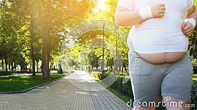 Obese man jogging in park, persistent in losing weight, big belly close up Stock Photo