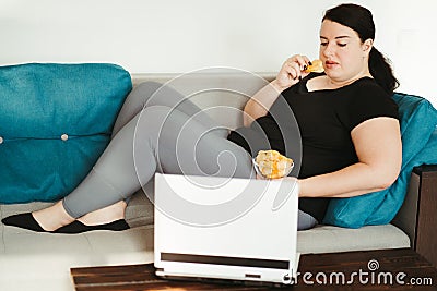 Obese woman sitting on sofa eating unhealthy food Stock Photo