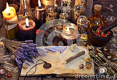 Open book with healing herbs, lavender flowers, candles, potion bottles and magic objects Stock Photo