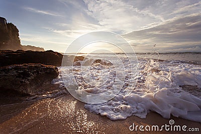 Ocean wave with foam beating against the rocks at sunset Stock Photo