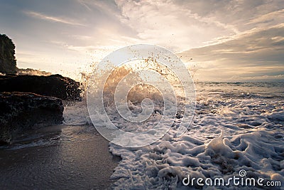 Ocean wave with foam beating against the rocks at sunset Stock Photo