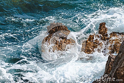 Ocean waves braking at coastline rocks covering them in white sea foam Stock Photo