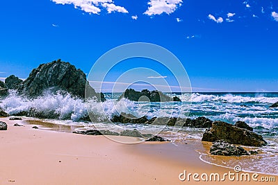 Ocean waves breaking on beautiful rugged rocks on the beach on bright sunny day. Stock Photo