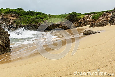 Clean beach sand with ocean waves plashing the shore rocks Stock Photo