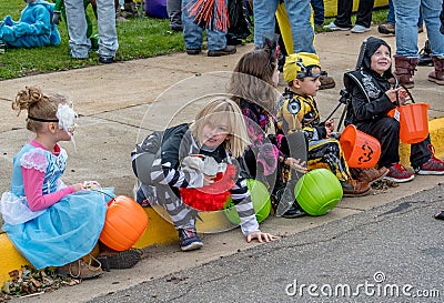 A row of children dressed in fun Halloween costumes, sit on a curb waiting for the parade for Editorial Stock Photo