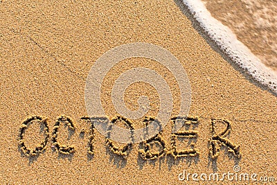 October - word drawn on the sand beach with the soft wave. Stock Photo