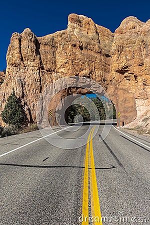Yellow line divides Utah state highway and drives through Red Rock with hole in center Stock Photo