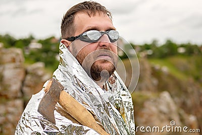 An oddball in glasses with an axe in his hand and dressed in foil against the sky Stock Photo
