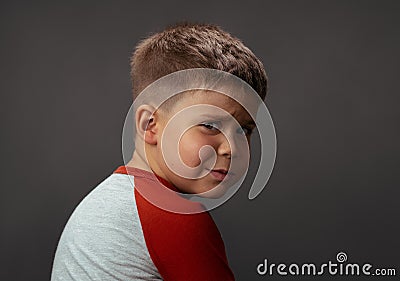 Offended child looks into the camera from behind his back. Crying boy in studio on an isolated background. High quality Stock Photo