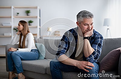 Offended mature man and woman sitting on different sides of sofa after after quarrel indoors, empty space Stock Photo