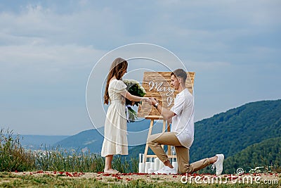 Offer in the mountains. A guy puts a ring on his bride while standing on his knee. Happy couple. Marry me. Good luck with the Stock Photo