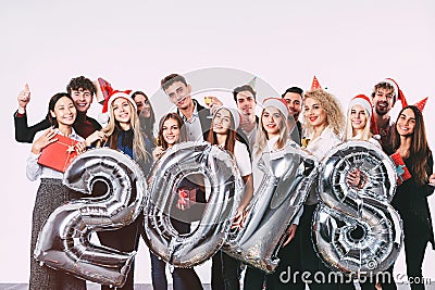 Office christmas party 2018. Group of cheerful young people in Santa hats holding silver colored number balloons. Stock Photo