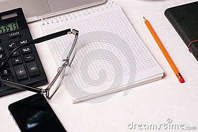 Office Desk of a company employee or workplace at home. Calculator, glasses, Notepad with a blank page, mobile phone. Accounting Stock Photo