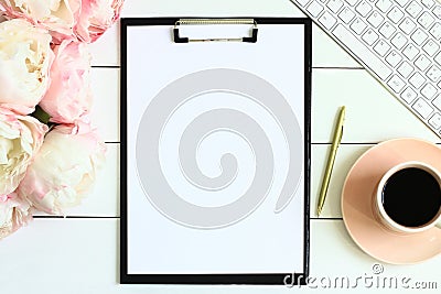 Office desk table with cup of coffee, pink peony flowers, golden pen, blank paper and clipboard. Stock Photo