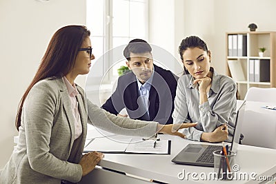 Real estate agent showing young couple different house variants on laptop screen Stock Photo