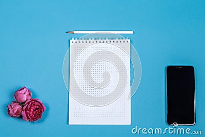Office table desk with tablet, smartphone, flowers and white blank notepad on blue. Top view and copy space for text Stock Photo