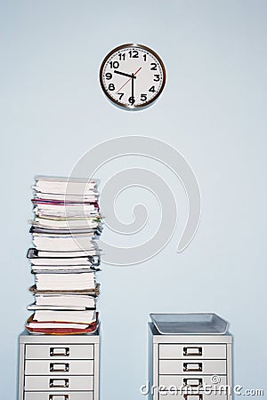 Office wall with clock stack of paperwork in inbox on file cabinet Stock Photo