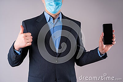 Office worker with mobile phone in protective mask on gray background Stock Photo