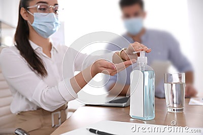 Office worker in protective mask using sanitizer at table, focus on hands. Personal hygiene during COVID-19 pandemic Stock Photo