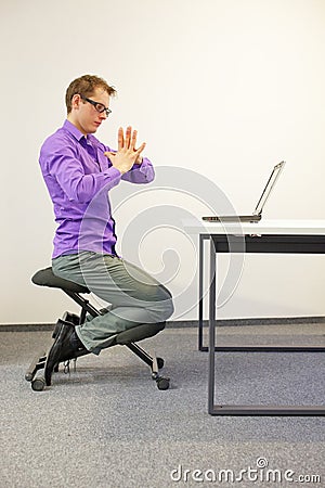 Office worker sitting on kneeling stool, exercising during short break in work Stock Photo