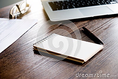 Office workspace with blank notebook , pen , paper sheet and laptop on the wooden table with warm fall colors and soft-focus. Stock Photo