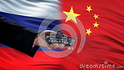 Official hand holding toy tank against Russia and China flag, armed attack Stock Photo
