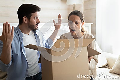 Confused shocked millennial spouses opening delivery with spoiled defective goods Stock Photo