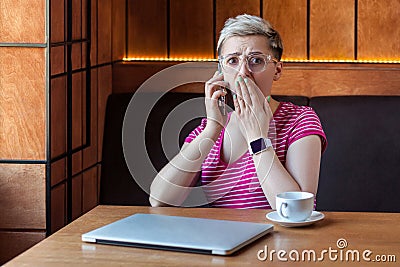 Oh my God! Portrait of unbelievable shocked young bussineswoman with short hair in pink t-shirt and eyeglasses is sitting in cafe Stock Photo