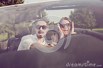 Oh no! Wtf! Front view, windscreen, guy grabs steering wheel while lady driver is panicking, both well dressed, in black trendy e Stock Photo