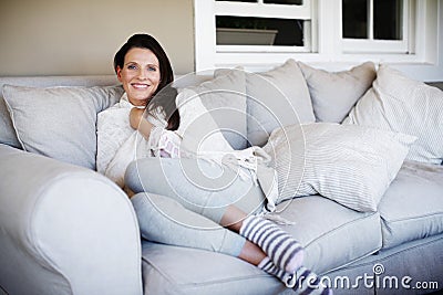 Oh so snug. Portrait of an attractive woman sitting snugly on a couch in a living room. Stock Photo