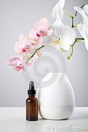 Oil diffuser with glass amber bottle and orchid flowers on white table Stock Photo