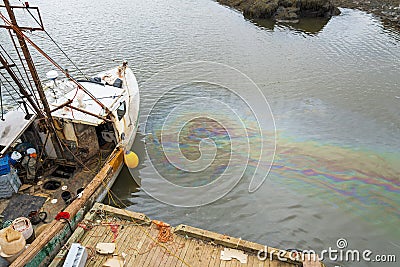 An oil slick in the water next to a fishing boat Stock Photo