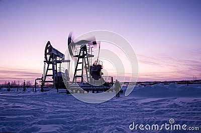 Oil worker in oilfield. Pump jack and engineer on a winter sunset sky background. Western Siberia. Stock Photo