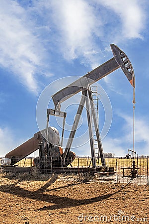 Oilfield pump jack out in summer red dirt field on bright day with shadow and a few whispy clouds in blue sky Stock Photo