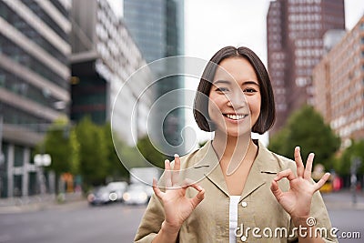 Okay, no problem. Smiling young asian woman shows ok gesture, approve smth, like and agree, accepting, standing on Stock Photo