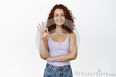 Okay, very good. Smiling redhead girl showing OK sign in approval, pleased, praise you, recommending smth, make Stock Photo