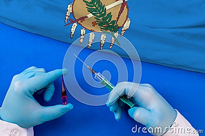 Hands of doctor holding syringe and coronavirus COVID-19 vial vaccine on flag Oklahoma Stock Photo