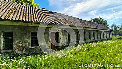 Old abandoned long house in poor condition. Bars and cracked panes in the windows. Around the tree and dandelions in the grass. Stock Photo