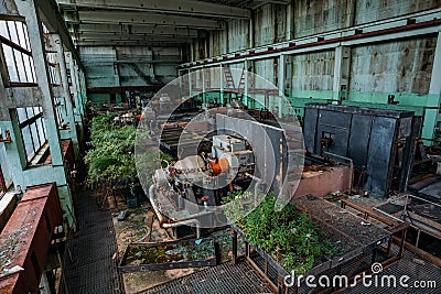 Old abandoned overgrown factory with rusty remains of industrial machinery in workshop Stock Photo