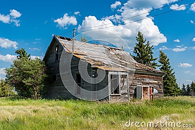 Old abandoned prairie farmhouse surrounded by trees, tall grass and blue sky Stock Photo