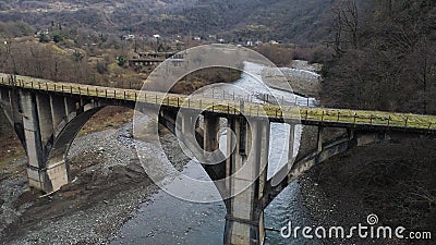 Old abandoned stone bridge over the cold mountainous river. Shot. Flying over rusty bridge and destroyed buildings amont Stock Photo