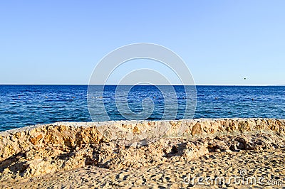 Old ancient yellow stone fence, a fence, a railings made of bristles, cobblestones covered with sand and a blue salt sea, an ocean Stock Photo