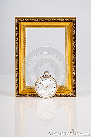 Old antique mechanical golden steel pocket watch in front of an empty wooden gold frame isolated on white background. Stock Photo