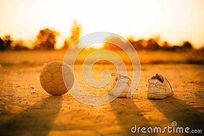 An old ball with the shoes for street soccer football under the sunset ray light. Stock Photo